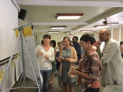 a group of people standing around an easel with one woman writing notes